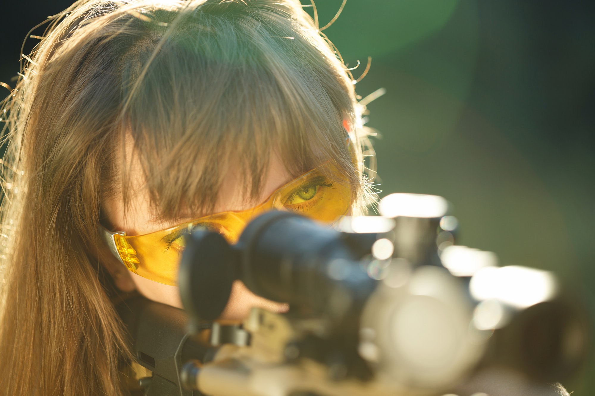 Girl with a gun for trap shooting and shooting glasses aiming at